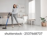 Young woman cleaning floor with cordless vacuum cleaner in bedroom