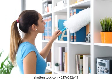 Young Woman Cleaning Her House, She Is Dusting A Bookcase, Chores And Hygiene Concept