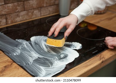 A young woman is cleaning an induction electric hob. Cleaning in the kitchen. Electric oven cleaning. Cleaning company concept. - Shutterstock ID 2110478099