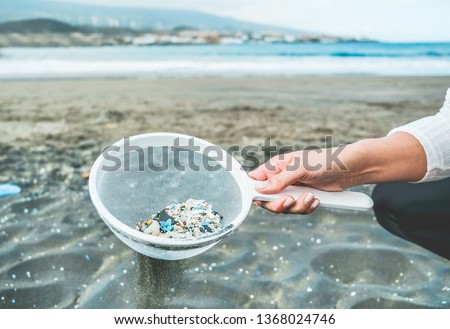 Young woman cleaning microplastics from sand on the beach - Environmental problem, pollution and ecolosystem warning concept - Focus on hand