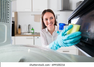 Young Woman Cleaning Microwave Oven With Spray Bottle And Sponge