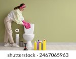 Young woman cleaning toilet bowl near green wall