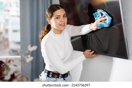 Young Woman Cleaning TV With Rag In Living Room At Home.