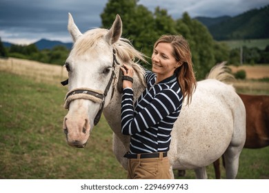 Young woman cleaning white gray horse with brush, her head next to animal - Powered by Shutterstock