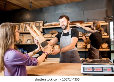Young woman client buying bread at the bakery shop with handsome male sellers - Powered by Shutterstock