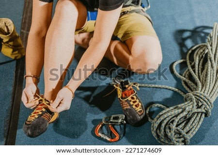 Young woman climber prepare before to climbing on the boulder wall indoor with equipment, shoe, rope, carabiner, concept of extreme sports and bouldering