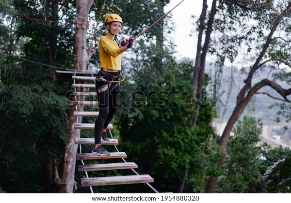 Young woman with climbing gear\
in an adventure extreme park climbing or passing on the rope\
road.