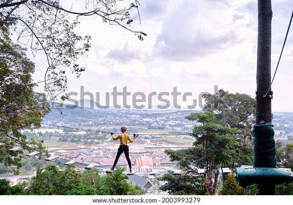 Young woman with\
climbing gear in an adventure extreme park passing on the high rope\
road with wonderful view.