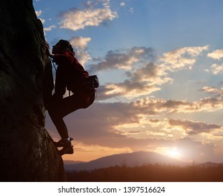 Young Woman Climbing High Up On Rock At Sunset In Mountains. Cloudy Sky On Background. Side View. Copy Space For Text. Difficult Ascent To Mountain Top. Extreme, Hiking, Overcoming Obstacles Concept.