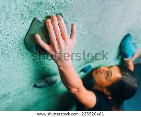Young woman climbing up on wall in gym, focus on hand