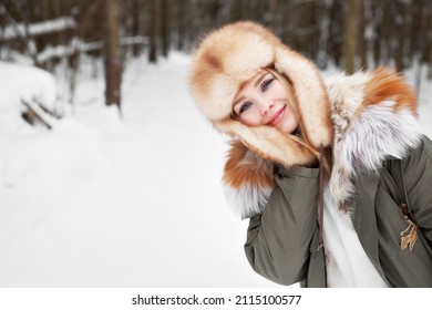 Young woman close up portrait at winter nature background, wearing parka jacket, fur hat and bright leather gloves, healthy activity. Blonde girl with blue eyes and beautiful smile