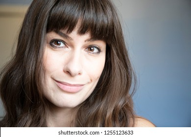 Young woman close-up portrait. Caucasian with brown long hair and bangs. Smiling expression, looking right. Copy space