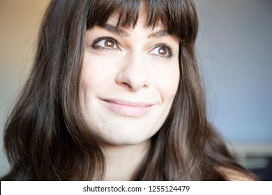 Young woman close-up portrait. Caucasian with brown long hair and bangs. Smiling expression, looking up left.