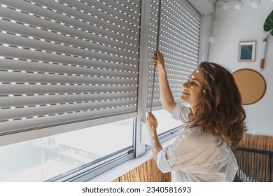 Young woman closing roller shutters on the balcony on a summer day