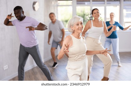 Young woman coach rehearsing with group of multinational sports aged people modern dance in dance hall - Powered by Shutterstock