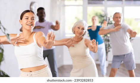 Young woman coach rehearsing with group of multinational sports aged people modern dance in dance hall - Powered by Shutterstock