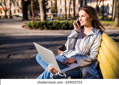 Young woman in coat working with laptop and phone on the bench in the city - Powered by Shutterstock