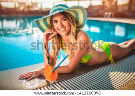 Young woman with cocktail glass chilling in the tropical sun near swimming pool 