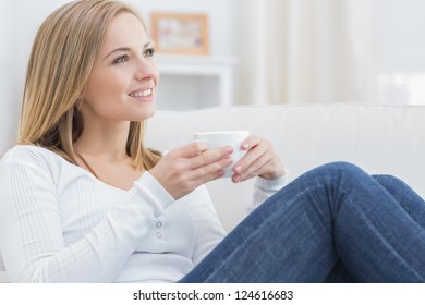 Young Woman With Coffee Cup Day Dreaming On Couch At Home