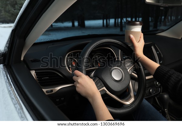 Young woman with coffee driving car along winter\
forest, closeup