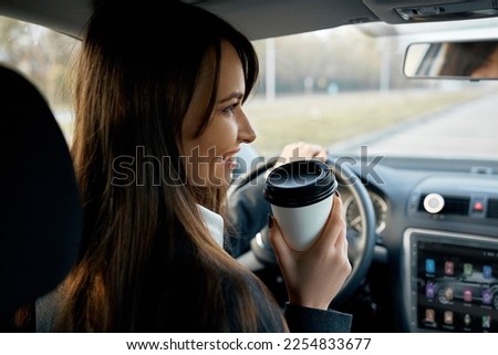Young woman with coffee to go driving her car.