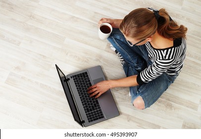 Young woman with coffee mug sitting on the floor with laptop. Concept of distant work, lifestyle and technology.
