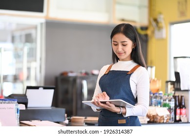 Young Woman Coffee Shop Owner Wearing Apron Holding Digital Tablet Ready To Receive Orders.