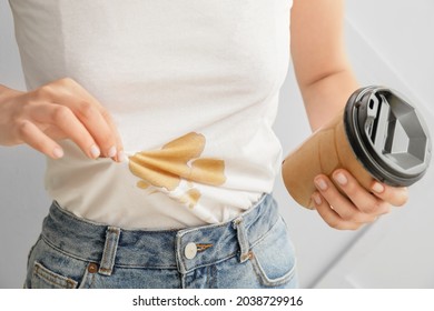 Young woman with coffee stains on her t-shirt on light background, closeup