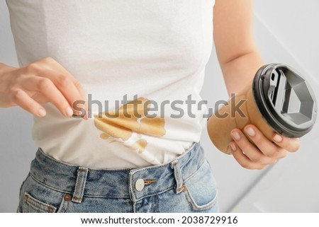 Young woman with coffee stains on her t-shirt on light background, closeup