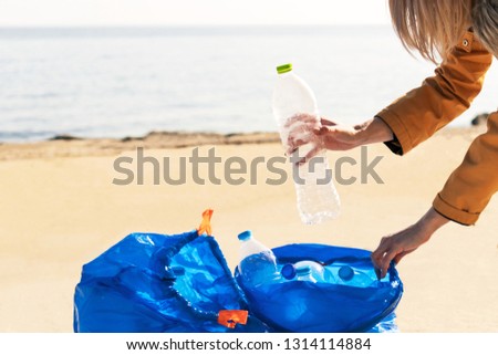 Young woman collecting plastic trash from the beach and putting it into blue plastic bags for recycle. Cleaning and recycling concept.