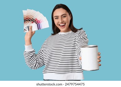 Young woman with color palettes and can of paint on blue background - Powered by Shutterstock