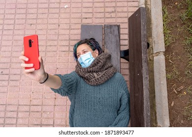 A Young Woman With Colorful Hair Wearing Snood And Sweater Taking A Selfie Wearing A Sanitary Mask