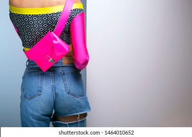 Young Woman Colorful Long Sleeve Top And Magenta Fanny Pack, 80s Fashion Look With High Waist Ripped Jeans, Back View