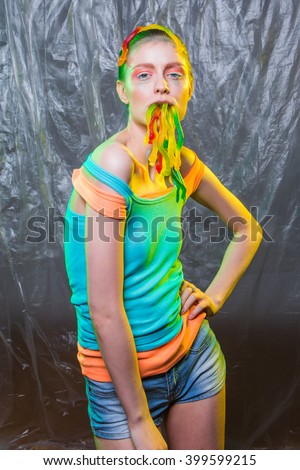 Young woman with colorful make up holds gummy jelly worms candies in mouth.