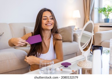Young woman combing hair. Young woman brushing healthy hair in front of a mirror. Combing her hair to keep it healthy. Close-up of beautiful young woman brushing her long hair and looking away