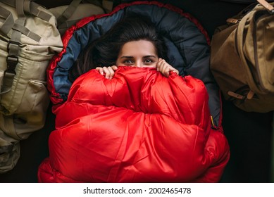 A young woman in a comfortable sleeping bag in a tent, top view. A tourist in a sleeping bag. A traveler wrapped in a red sleeping bag. Travel, camping concept, adventure. Traveling with a tent