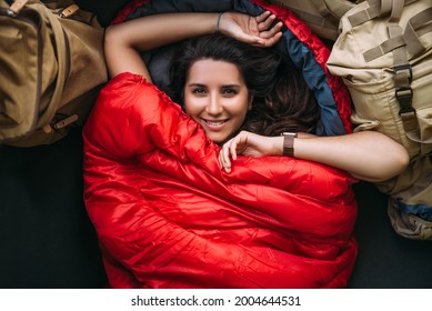 A young woman in a comfortable sleeping bag in a tent, top view. A tourist in a sleeping bag. A traveler wrapped in a red sleeping bag. Travel, camping concept, adventure. Traveling with a tent - Powered by Shutterstock