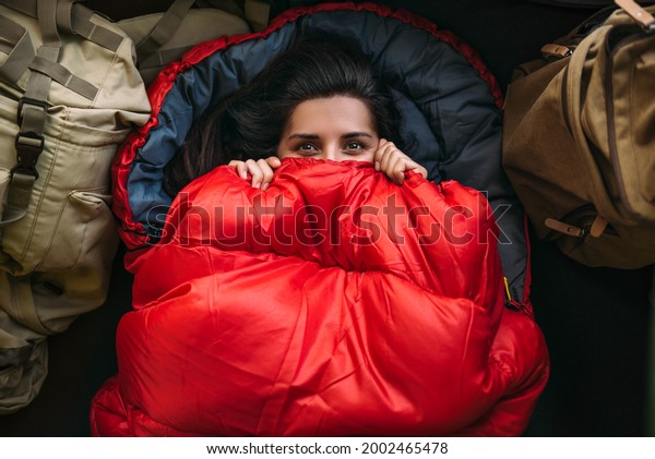 A young woman in a comfortable sleeping bag in a
tent, top view. A tourist in a sleeping bag. A traveler wrapped in
a red sleeping bag. Travel, camping concept, adventure. Traveling
with a tent