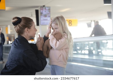 Young woman comforting child lost at the airport who can't find her parents. Mother consoling upset little crying girl which got scared from flight at the airport.