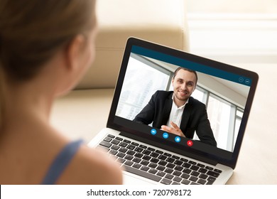 Young woman communicating with man in formal suit via video call application. Young couple chatting. Long distance relationship, virtual communication. Close up view over shoulder, focus on screen.