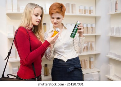 Young Woman Comparing Cosmetics Products With Saleswoman In A Drugstore