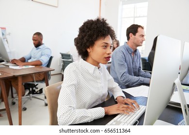 Young woman at computer with colleagues in open plan office - Shutterstock ID 656511364