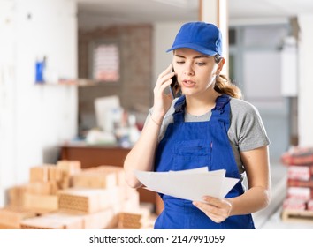 Young Woman Construction Worker Standing In Construction Site, Holding Documents And Talking On Phone.