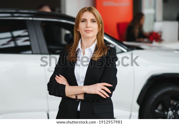 Young\
woman consultant in show room standing near\
car
