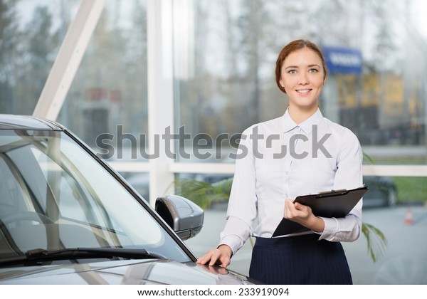 Young\
woman consultant in show room standing near\
car