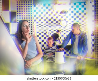 Young Woman Contemplating Solving Puzzle In Quest Room Stylized Under Chessboard While Having Fun With Her Family. Toned Image With Visual Effects