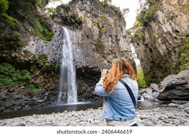 young woman contemplating and taking photos with her cell phone of the Texolo Waterfall very close to the beautiful magical town of Xico