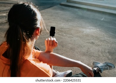 Young Woman Content Creator Streaming While Training At An Urban Scenario. Shot From Behind