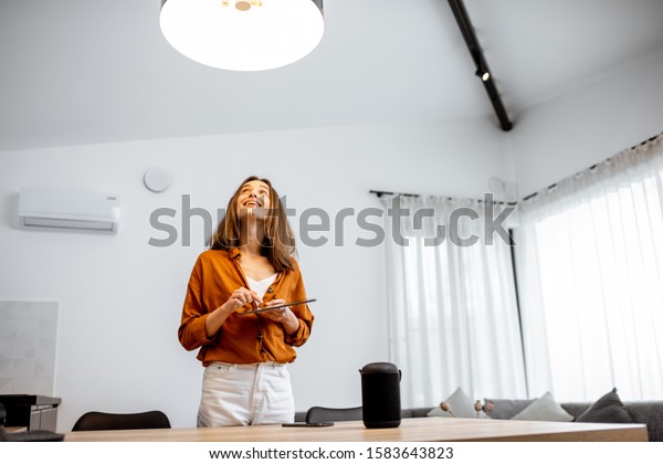 Young woman controlling home light with asmart\
home in the living room. Concept of a smart home and light control\
with mobile devices