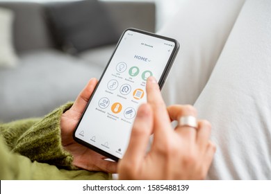 Young woman controlling home with a smartphone. Concept of a smart home and mobile application for managing smart devices at home - Shutterstock ID 1585488139